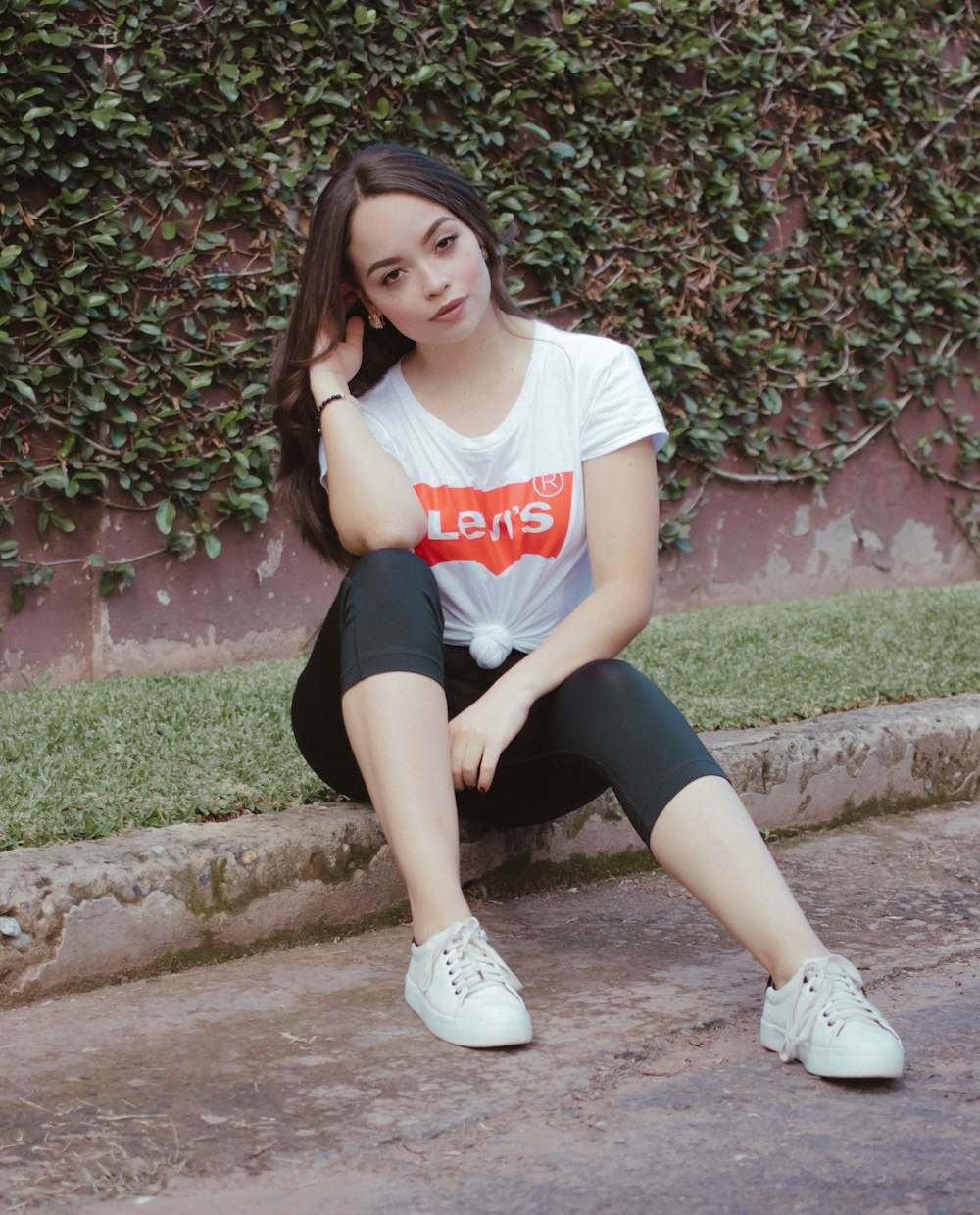 woman in white and red crew neck t-shirt and black shorts sitting on brown concrete