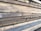 Multiple stacks of rough, unfinished wooden planks are piled horizontally, showcasing their natural grain and texture. The edges of the wood are uneven, with visible splinters and variations in color.
