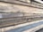 Multiple stacks of rough, unfinished wooden planks are piled horizontally, showcasing their natural grain and texture. The edges of the wood are uneven, with visible splinters and variations in color.