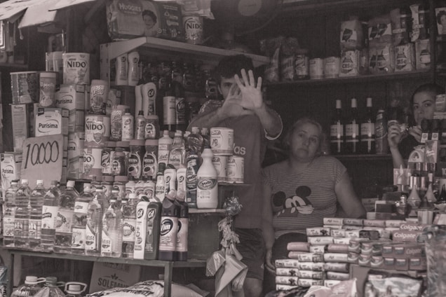 Photo of Cláudia Aparecida standing in front of her small local store with shelves of products visible inside.