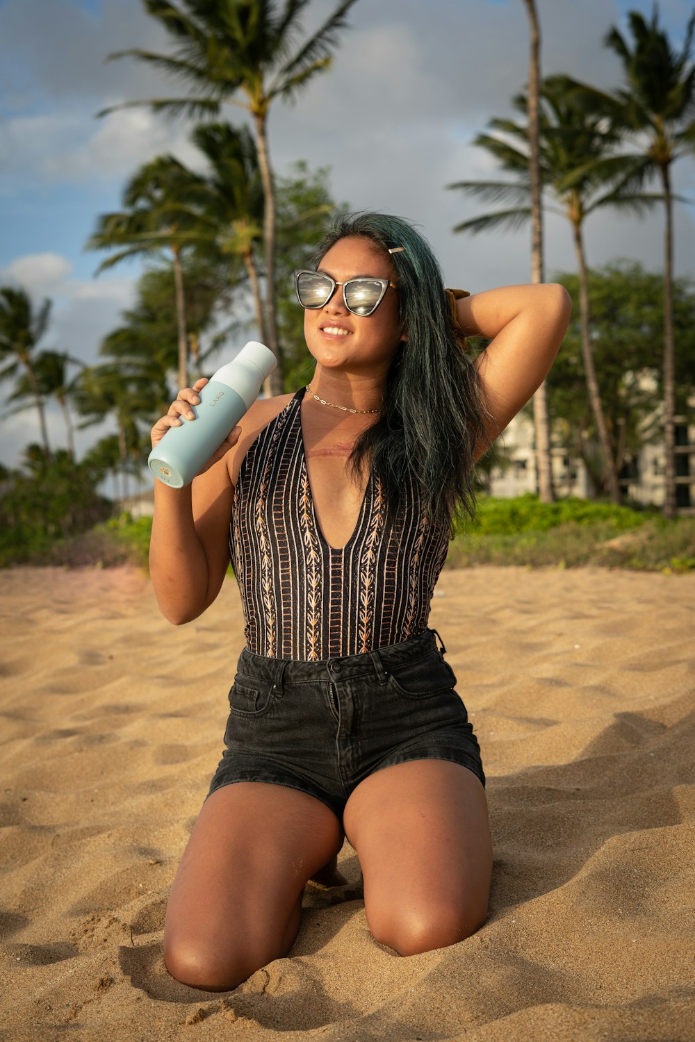 a woman sitting in the sand with a water bottle