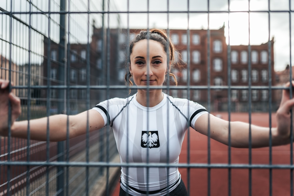 woman in white and black adidas crew neck t-shirt standing beside black metal fence during