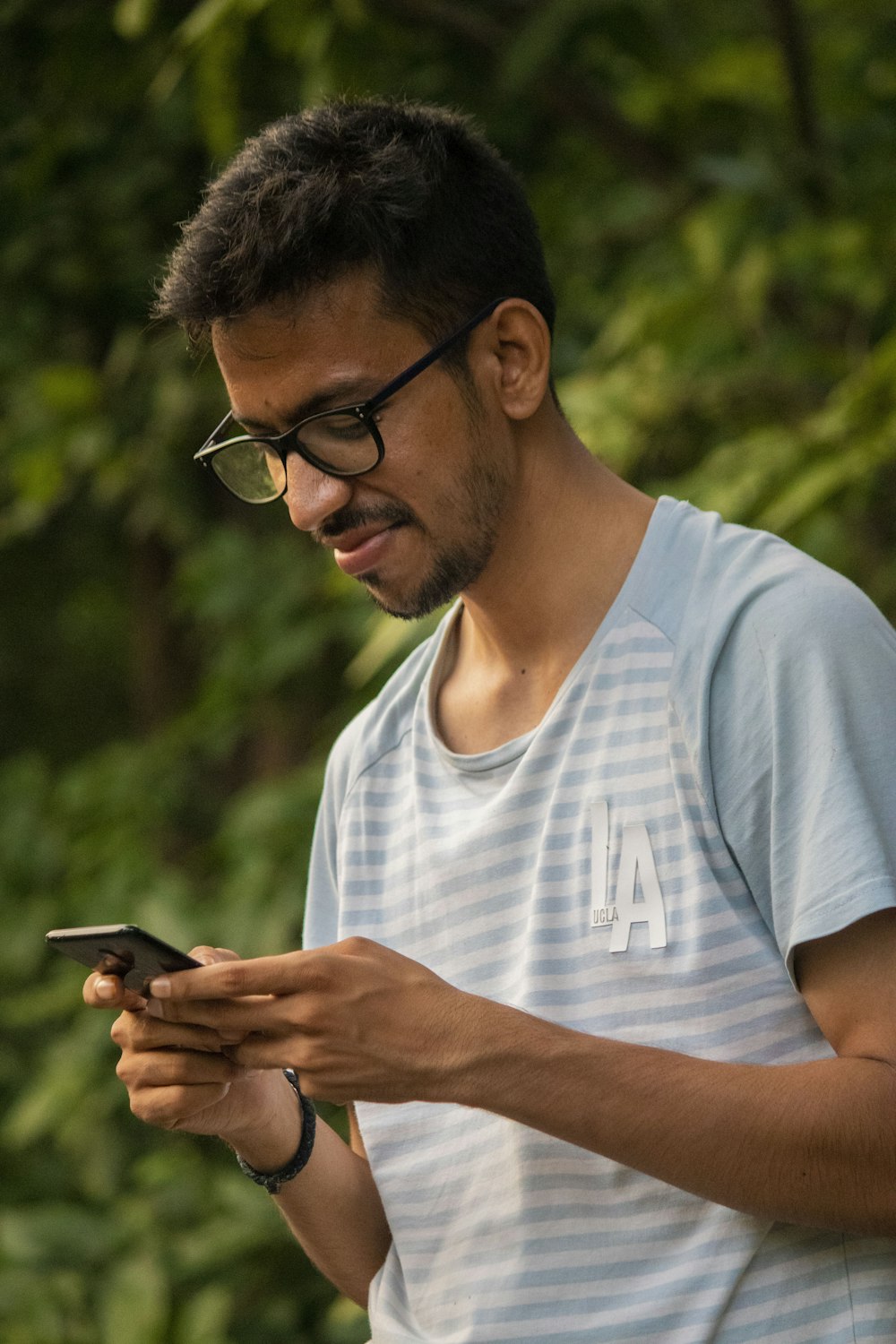 man in white crew neck t-shirt wearing black framed eyeglasses holding black smartphone