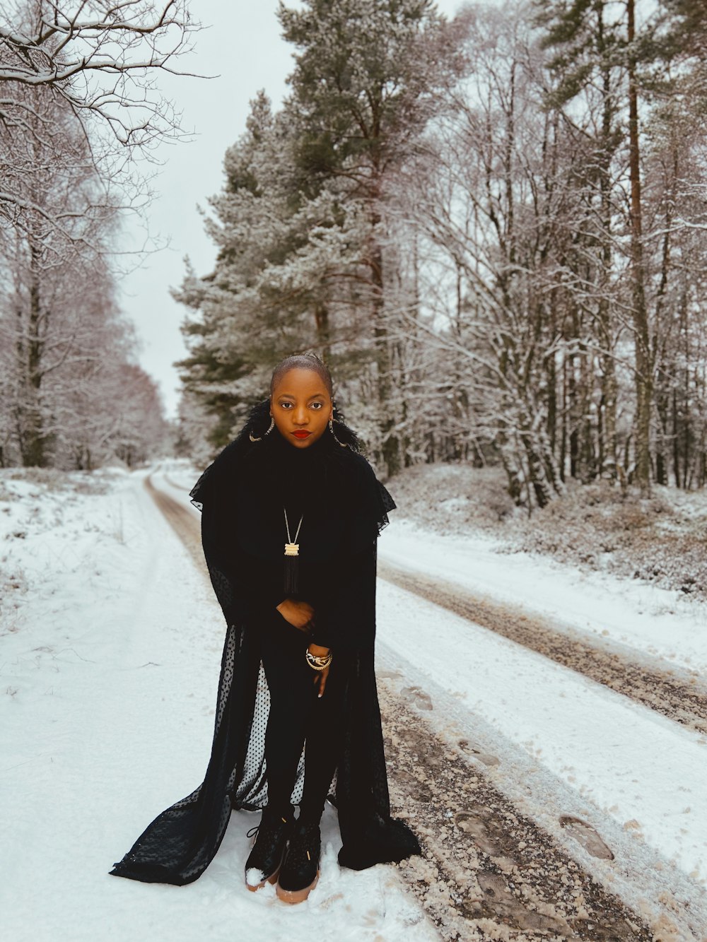 woman in black coat standing on road covered with snow during daytime