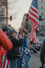 A group of diverse Americans standing united with flags and banners at a community rally.