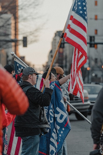 A group of diverse supporters holding American flags and Team Maga banners outdoors.