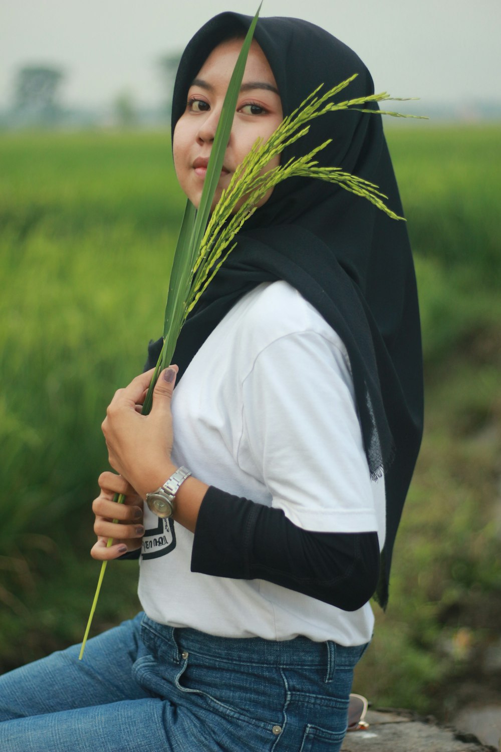 person in white shirt and black scarf holding green grass