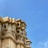 A detailed architectural structure with intricate carvings and designs adorns a corner of the building. The structure features ornate jharokhas and latticed windows, characteristic of traditional Indian architecture. The sky in the background is a vibrant blue, enhancing the aged elegance of the building.
