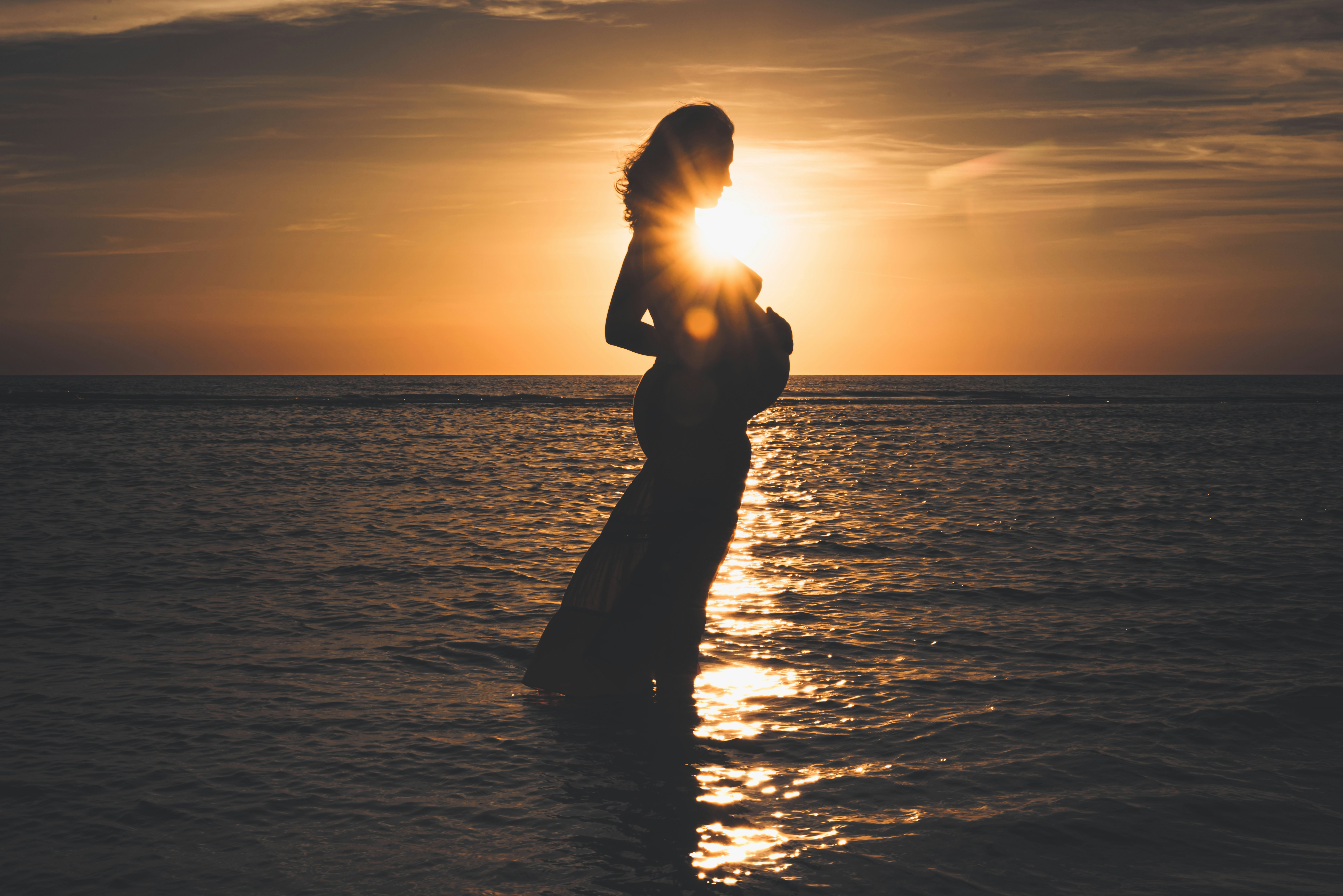 silhouette of man standing on sea during sunset