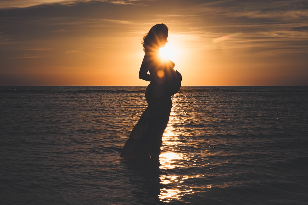 silhouette of man standing on sea during sunset