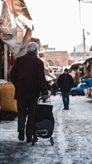 man in brown jacket and black pants holding black bag walking on street during daytime