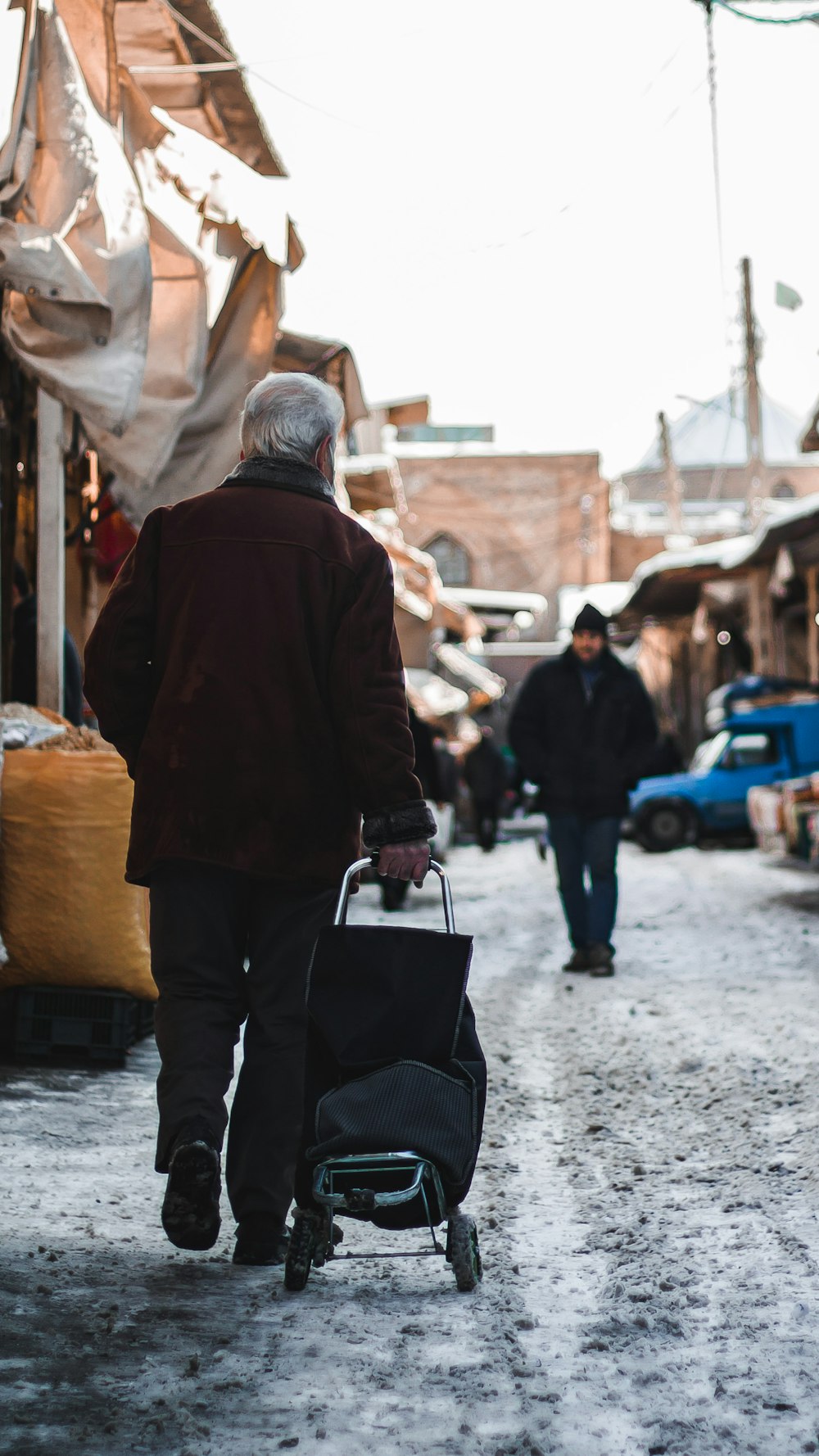 man in brown jacket and black pants holding black bag walking on street during daytime