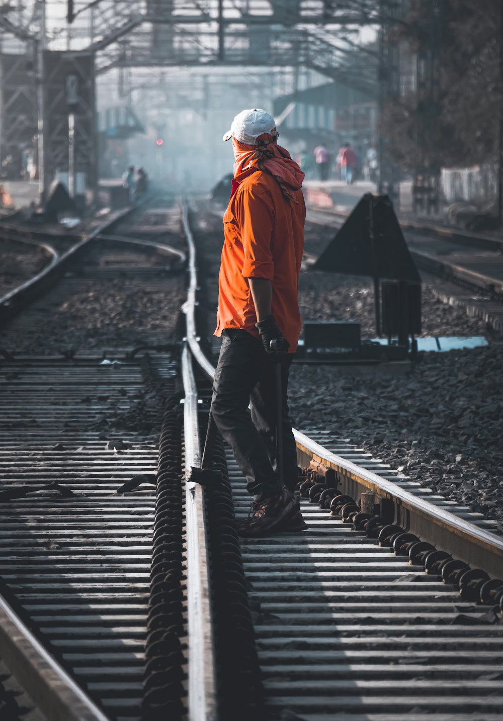 man in orange hoodie and black pants walking on train rail during daytime