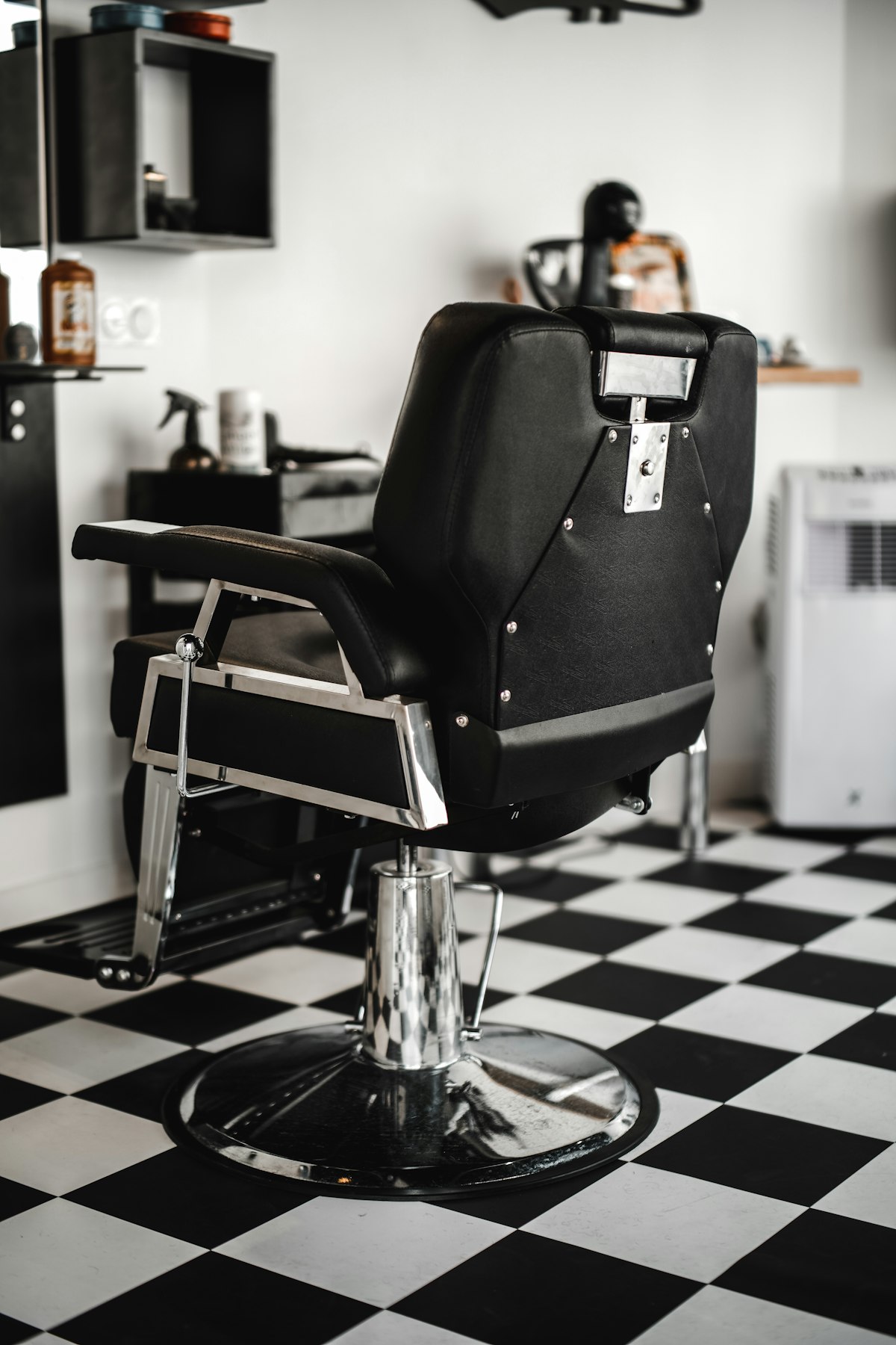 Empty black leather barber chair seen from behind on a black and white checkered floor