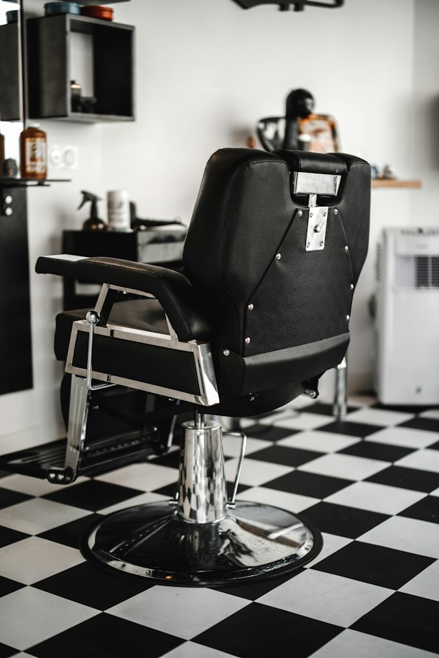 Empty black leather barber chair seen from behind on a black and white checkered floor