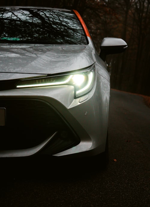 A silver car headlight illuminating a dark forest road