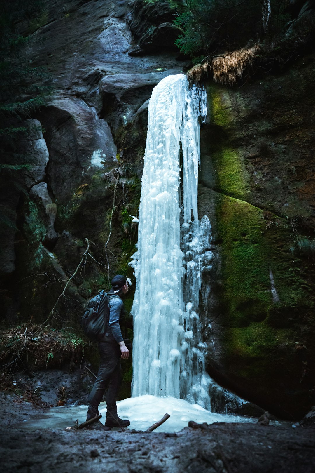 man in black jacket and black helmet standing in front of waterfalls during daytime