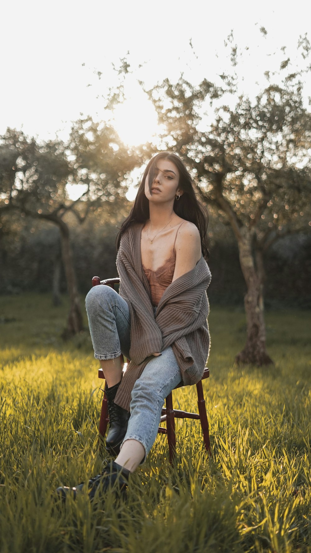woman in brown cardigan and blue denim jeans sitting on brown wooden chair on yellow flower