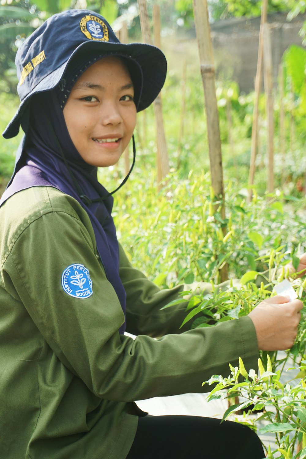 woman in green jacket and black hat holding green plant