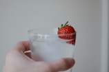 Close-up of a hand holding a glass of infused water with fresh herbs and citrus slices.