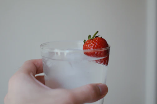 Close-up of a hand holding a glass of water next to fresh fruits