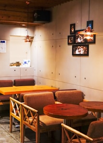 A cozy caf&eacute; interior with wooden tables and chairs, featuring a minimalist design. The walls are decorated with a cluster of framed coffee-themed photographs. Warm lighting suspended from the wooden ceiling adds a comforting ambiance.