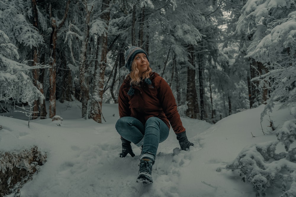woman in brown jacket and blue denim jeans sitting on snow covered ground