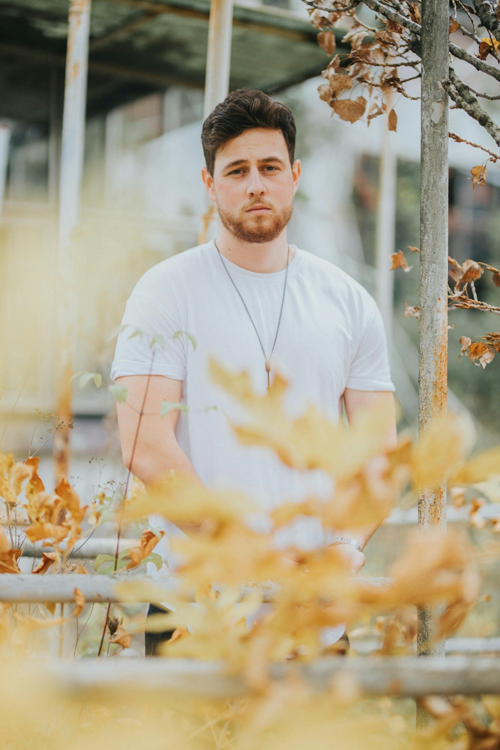 man in white crew neck t-shirt standing near brown wooden fence during daytime