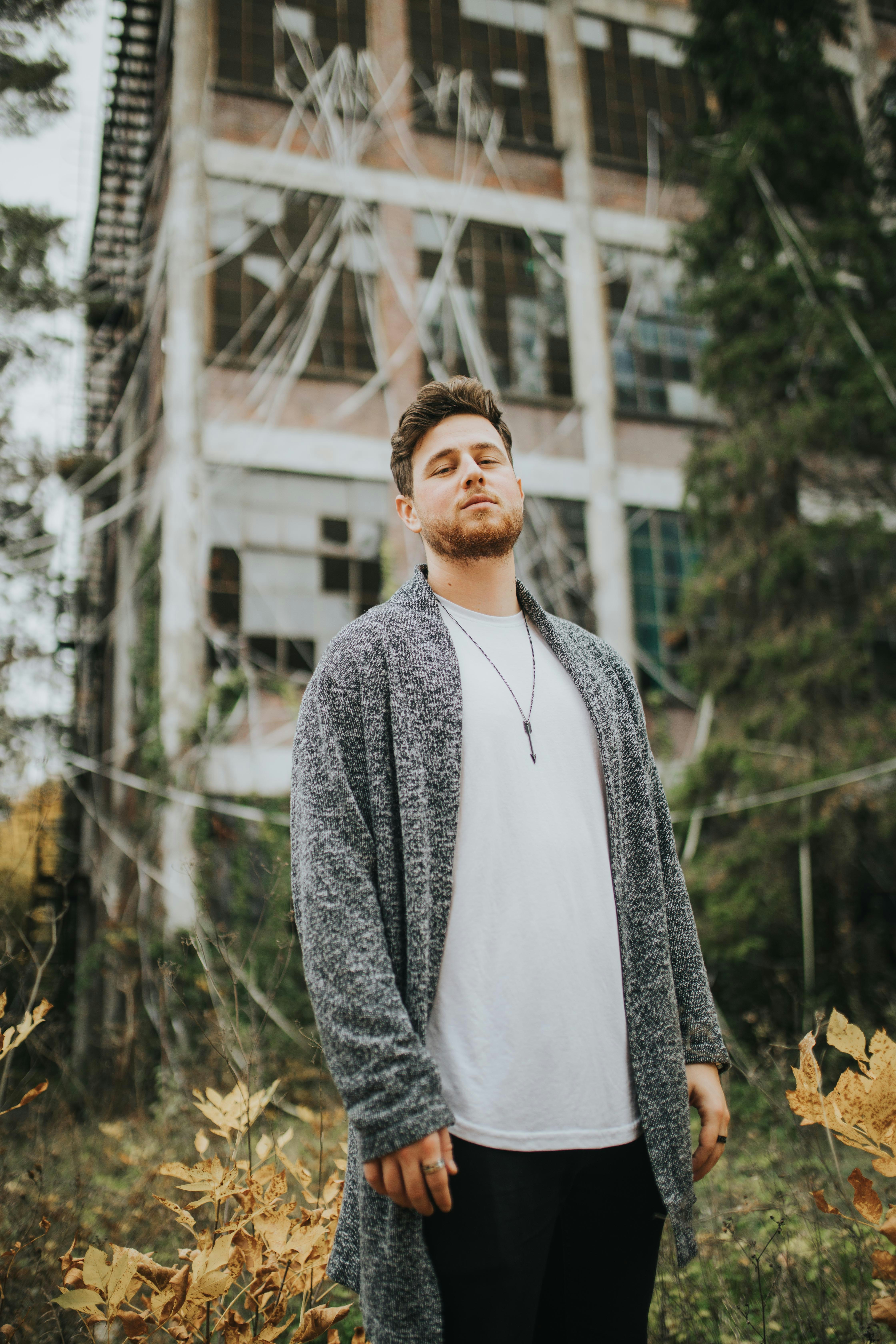 man in gray sweater standing near green trees during daytime