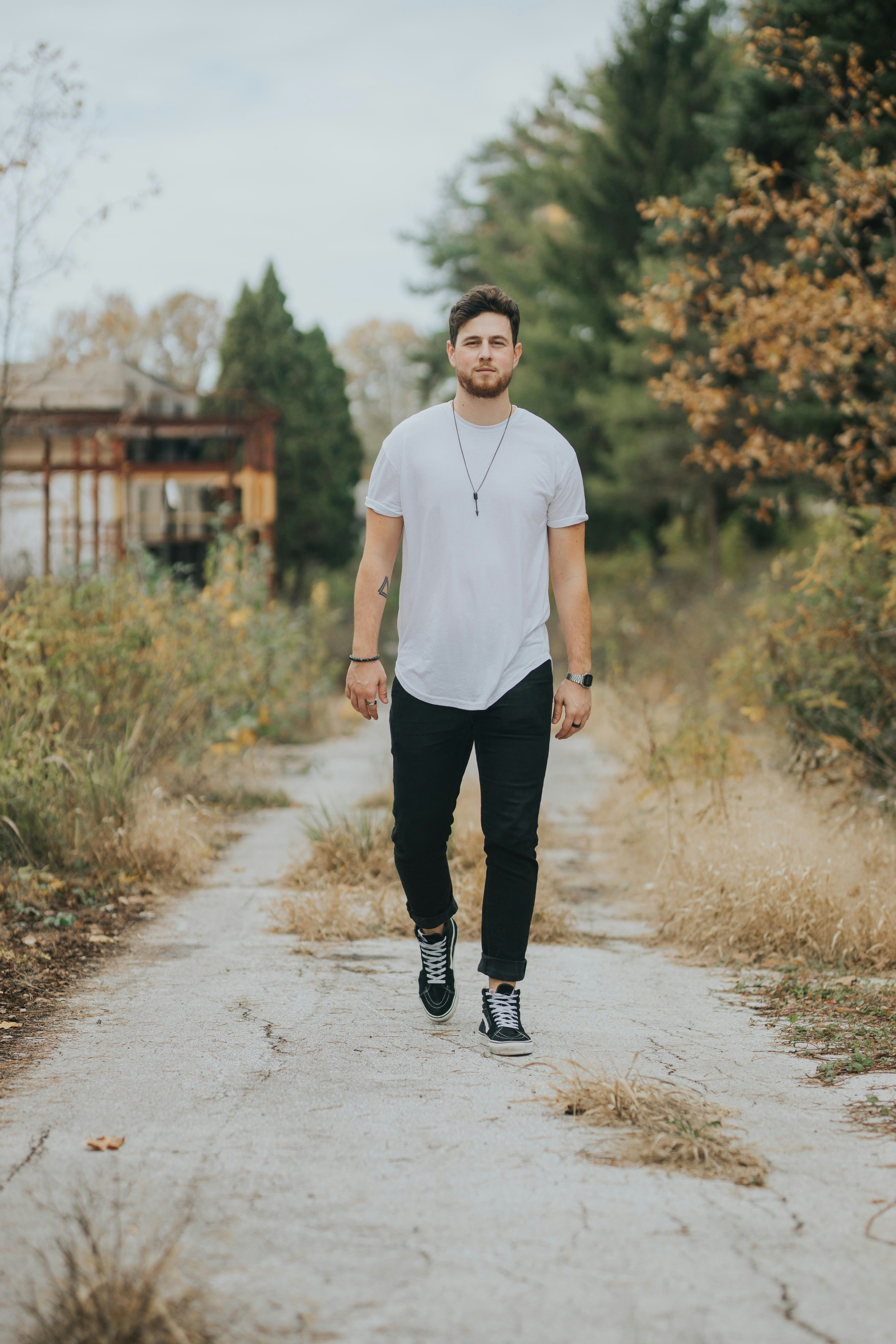 man in white tank top and black pants standing on road during daytime