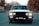 A vintage car with headlights on is positioned on a deserted road, surrounded by blurred foliage in the background with a soft focus. The license plate reads 'IDD 341', and the car's classic design features a prominent grille and wide headlights.