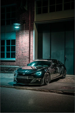 A sleek black sports car parked under moody lighting, highlighting its glossy finish.