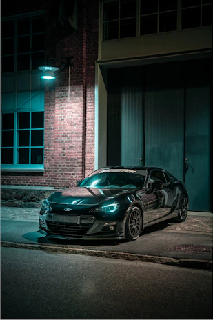 Sleek black noirveloce sports car illuminated by cinematic lighting on a dark urban street at night