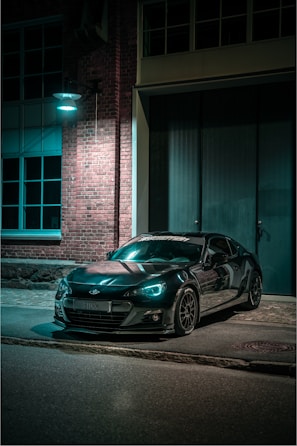 Sleek black sports car parked under moody blue lighting highlighting its curves.