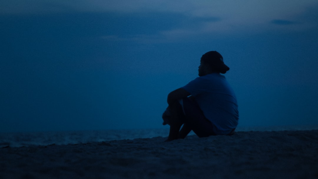 man in blue shirt sitting on gray sand during daytime