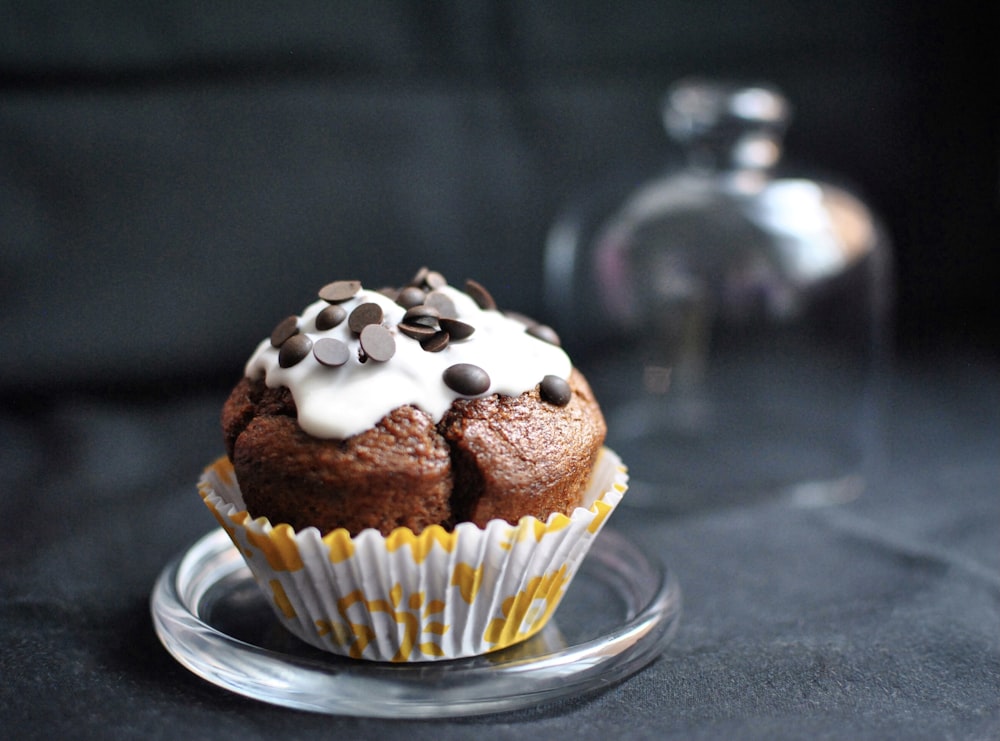 chocolate cupcake with white icing on clear glass saucer