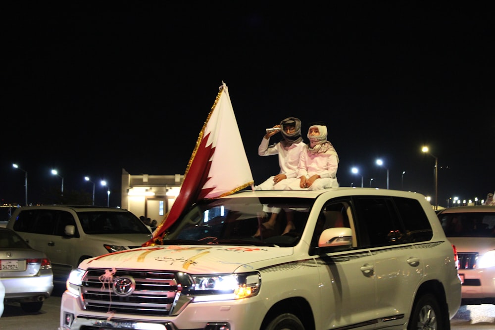 man and woman sitting on white suv during night time