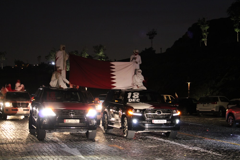 man in gray suit standing beside red and black car during night time