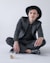man in black blazer and black pants wearing black hat sitting on floor