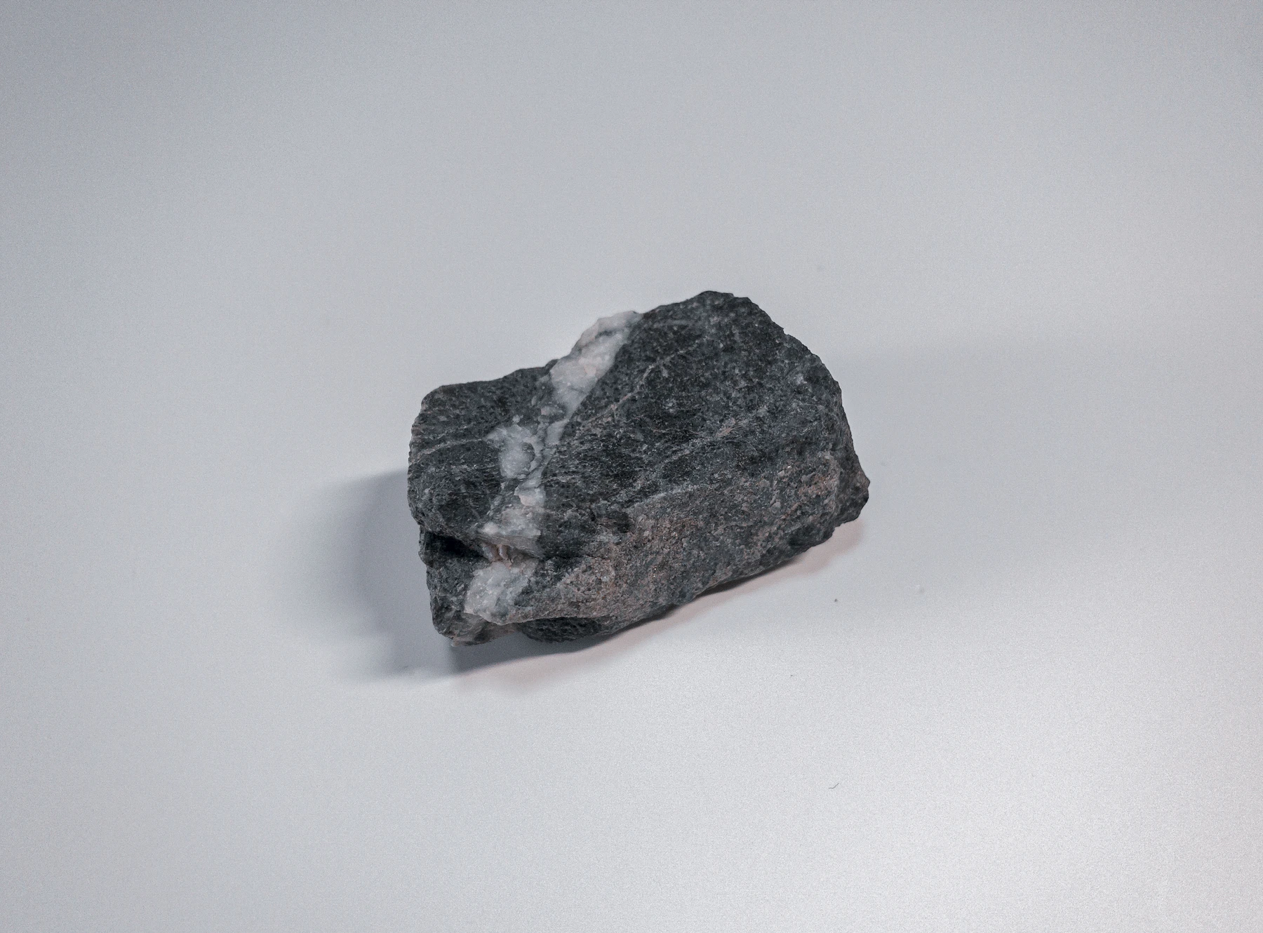A dark gray stone crossed by a white mineral vein, lying on a plain white surface