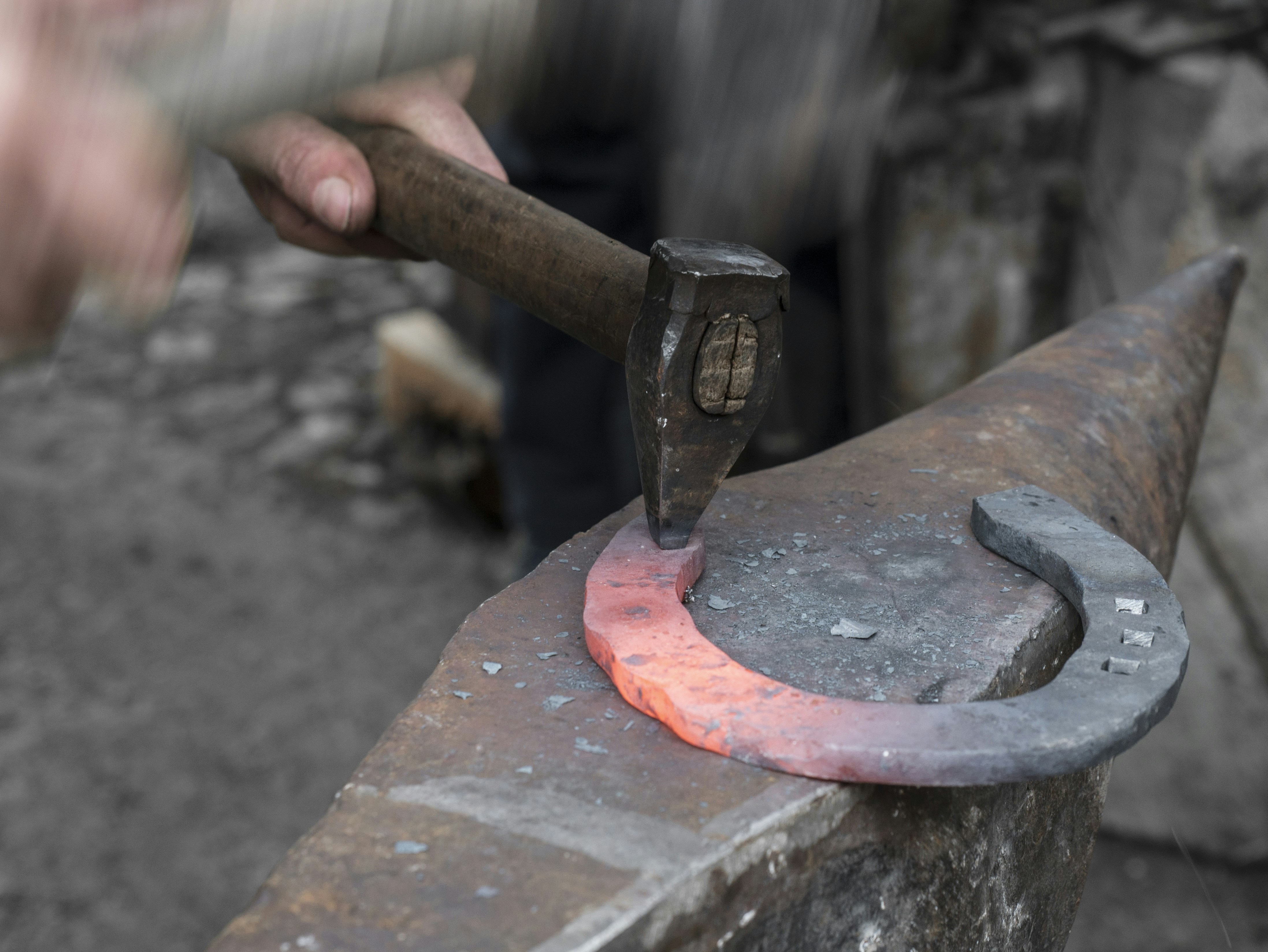 Horseshoe being shaped on anvil, glowing hot metal, dark workshop atmosphere, dramatic forge light
