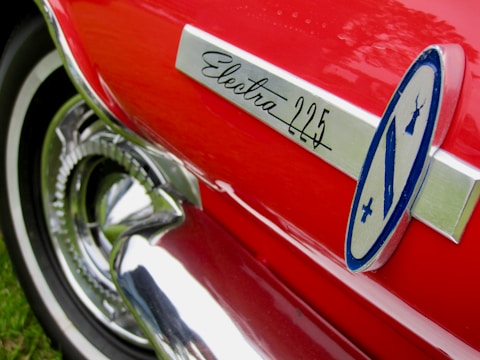 A close-up of a red car with a shiny chrome trim featuring the text 'Electra 225'. The image shows a part of a classic car's body including a stylized logo.
