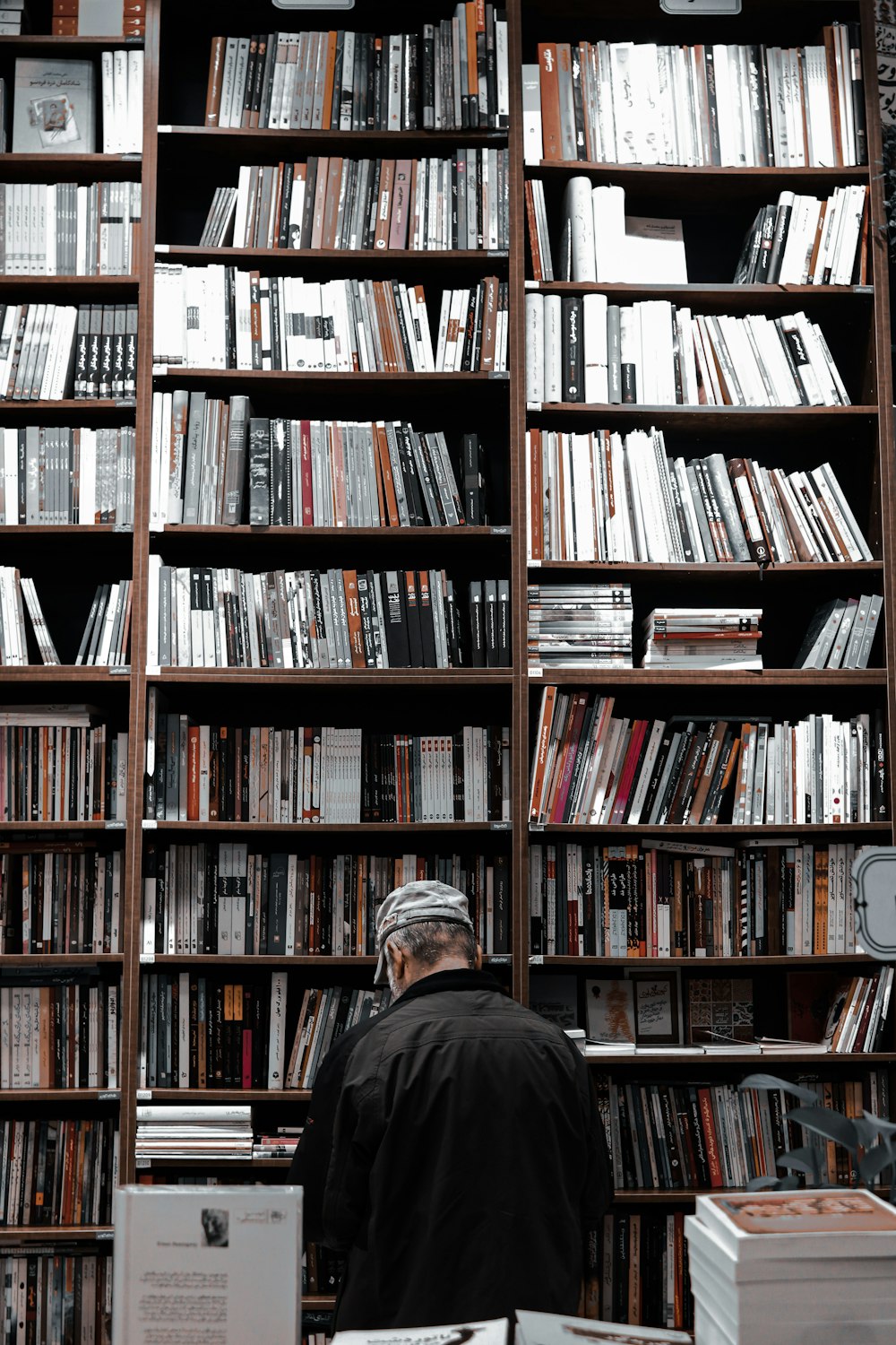 man in black jacket standing near brown wooden book shelves