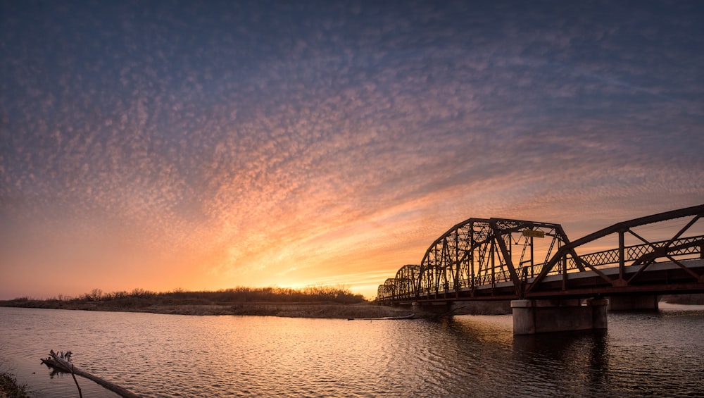 Puente de metal negro sobre el río durante la puesta del sol