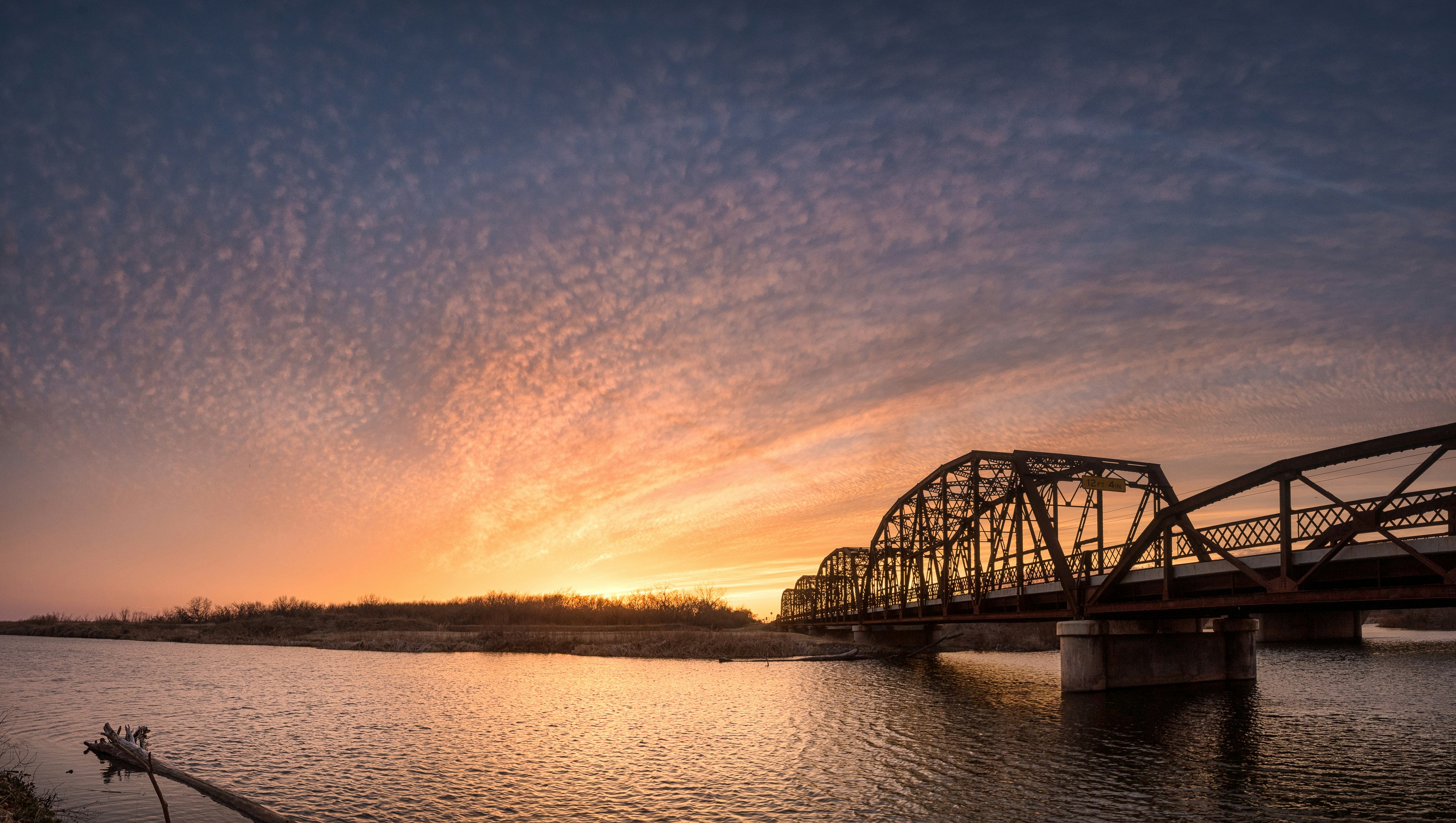 black metal bridge over the river during sunset