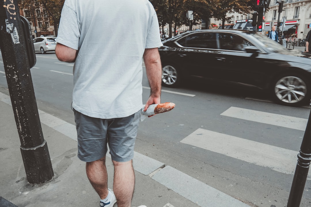 man in white crew neck t-shirt and blue denim shorts standing on sidewalk during daytime