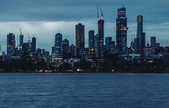 A modern urban skyline at dusk with cranes and illuminated high-rise buildings under construction.