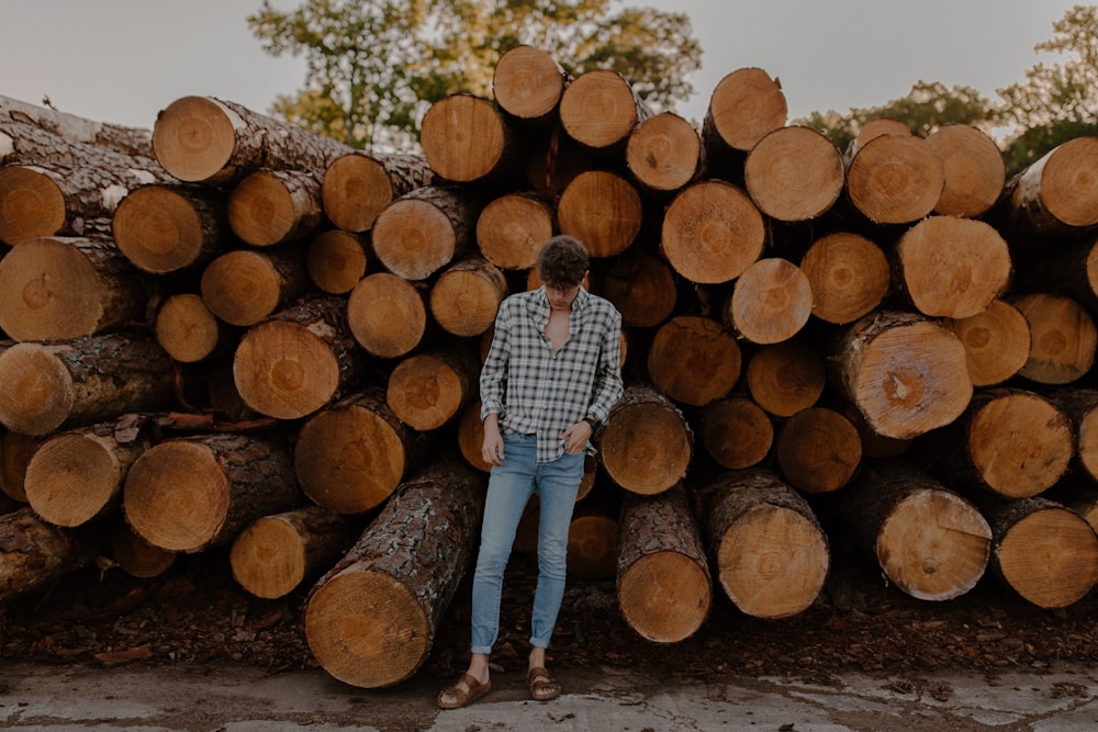 man in blue and white plaid dress shirt and blue denim jeans standing on brown tree