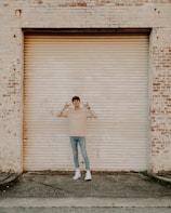 woman in white tank top and blue denim jeans standing beside brown wooden wall during daytime