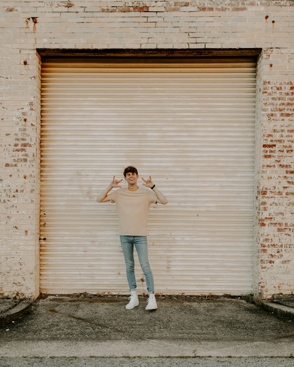 woman in white tank top and blue denim jeans standing beside brown wooden wall during daytime